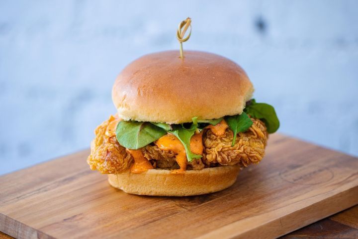 A fried chicken sandwich with spicy ranch sauce and spring mix on a potato bun.