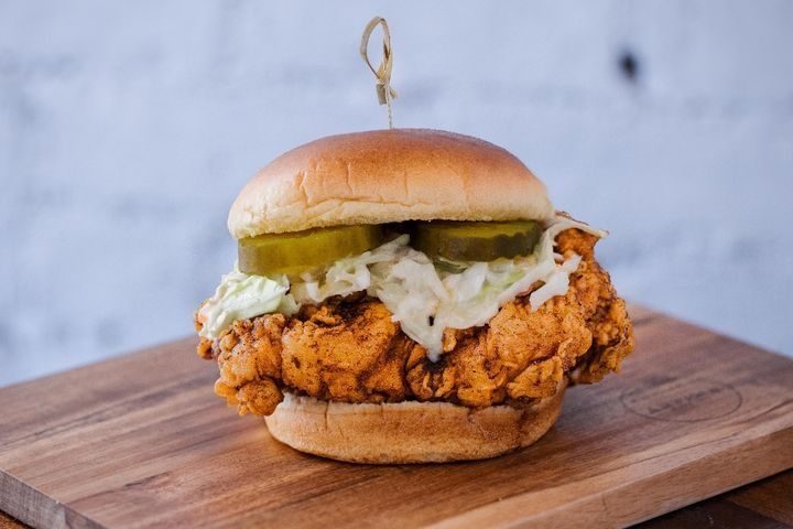 A Nashville Hot chicken sandwich with coleslaw and pickles on a potato bun.