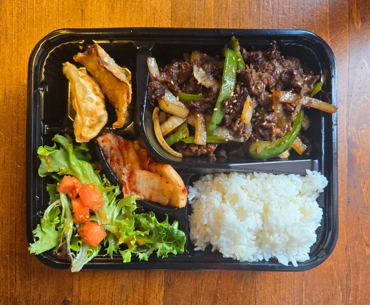 A lunch box with soy-marinated grilled beef with rice, mandu, salad, and kimchi.