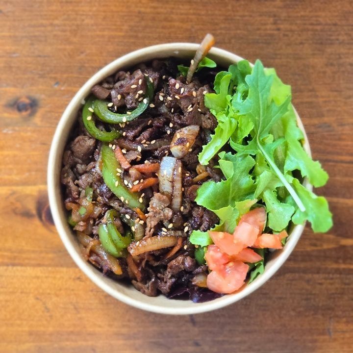 A bowl of soy-marinated beef over rice with salad and kimchi.