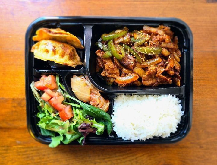 A lunch box with spicy marinated pork with rice, mandu, salad, and kimchi.