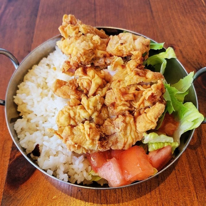 A bowl of fried chicken cutlet over rice and fresh greens.