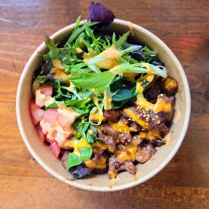A bowl of soy-marinated chicken over rice with salad and kimchi.
