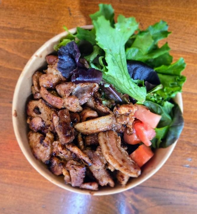 A bowl of soy-marinated pork over rice with salad and kimchi.