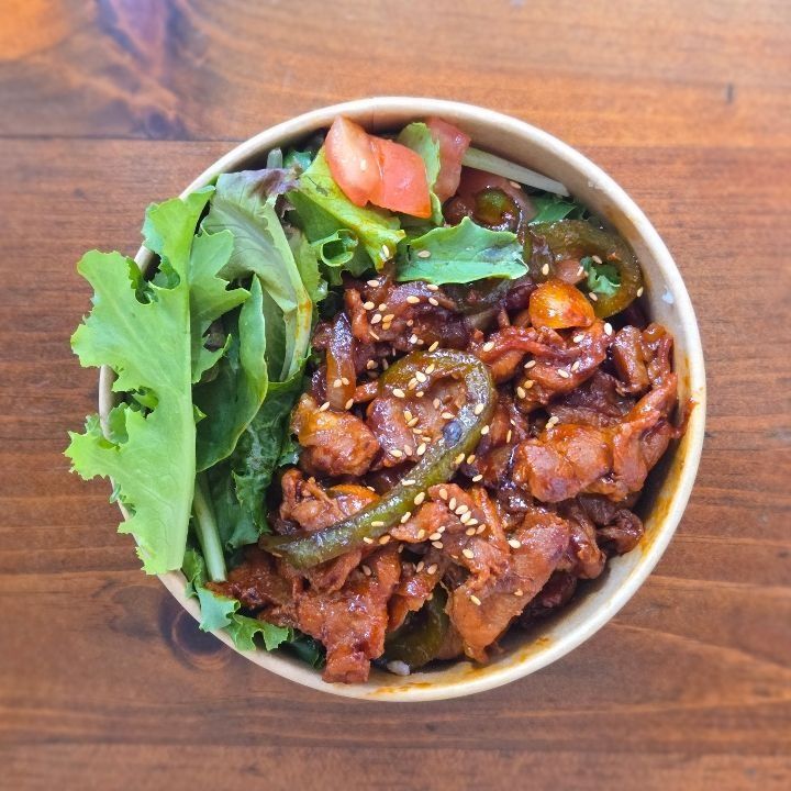 A bowl of spicy pork over rice with salad and kimchi.