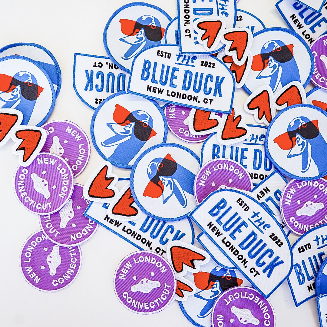 Image of multiple Blue Duck stickers showcasing variations in logo, illustration, and shape, highlighting the brand's diverse visual identity on a small-scale format.