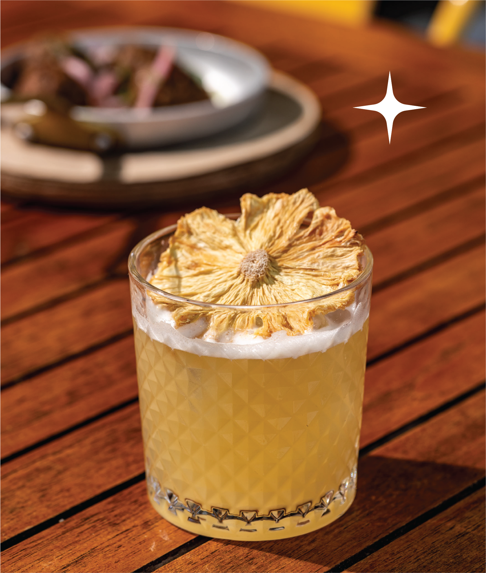 A visually appealing tropical cocktail in a textured glass, garnished with a dried pineapple wheel. The composition highlights the drink's color and texture against a wooden table.