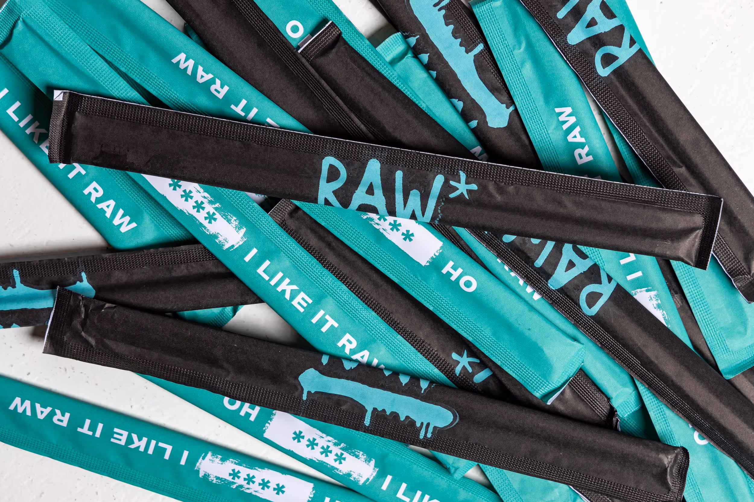  Detail-oriented view of RAW's packaging design, highlighting the contrasting teal and black color scheme, the prominent "RAW*" logo, and the playful tagline "I Like It Raw".