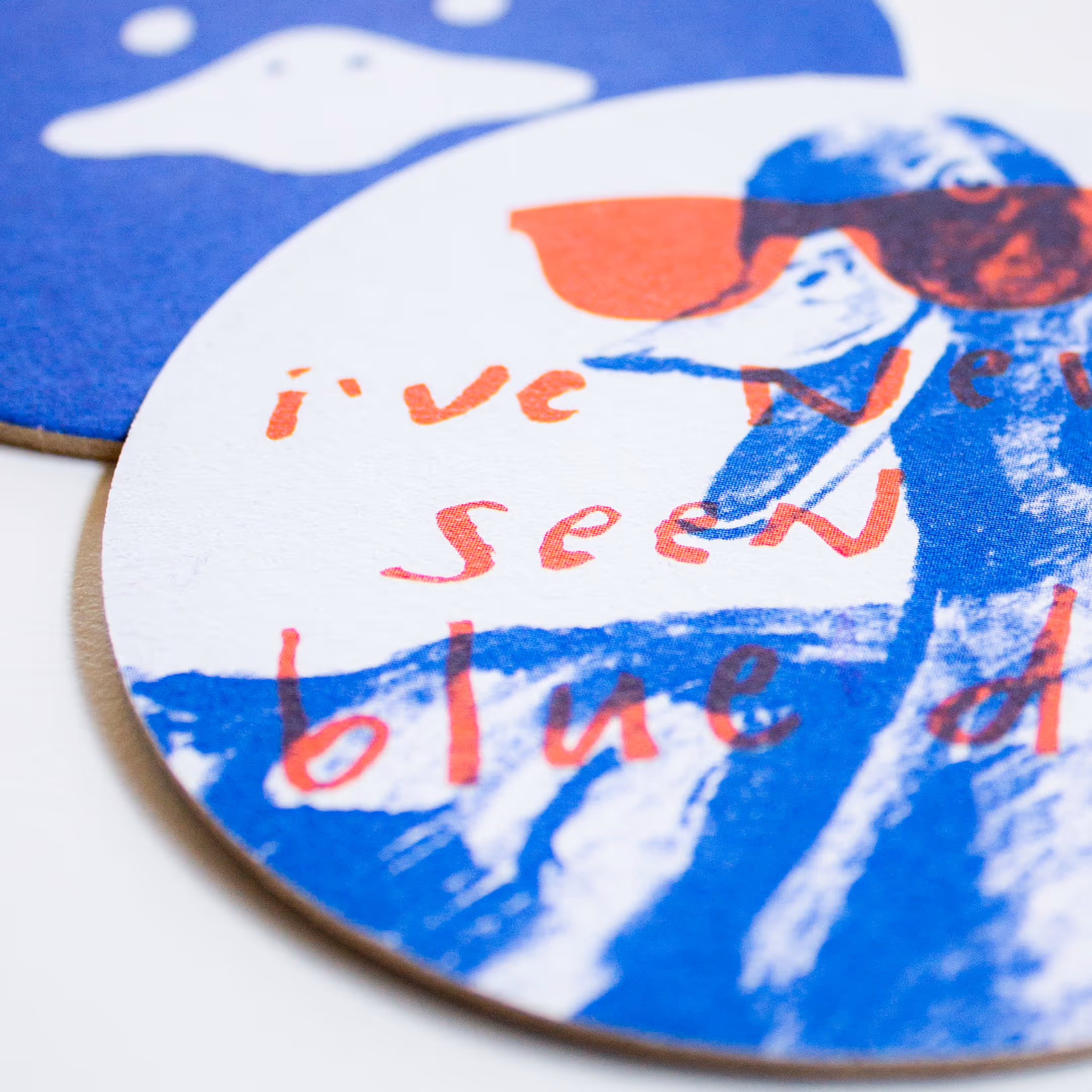 Close-up image of two overlapping Blue Duck Tavern coasters, showcasing the brand's logo and playful handwritten text against a blue and white color scheme.