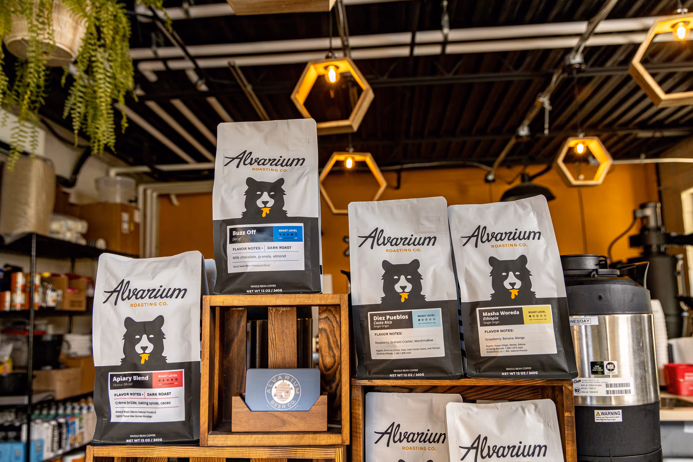 Image of various Alvarium Roasting Co. coffee bags arranged on wooden shelves, showcasing the brand's packaging design with its bear logo, typography, and color variations for different blends.