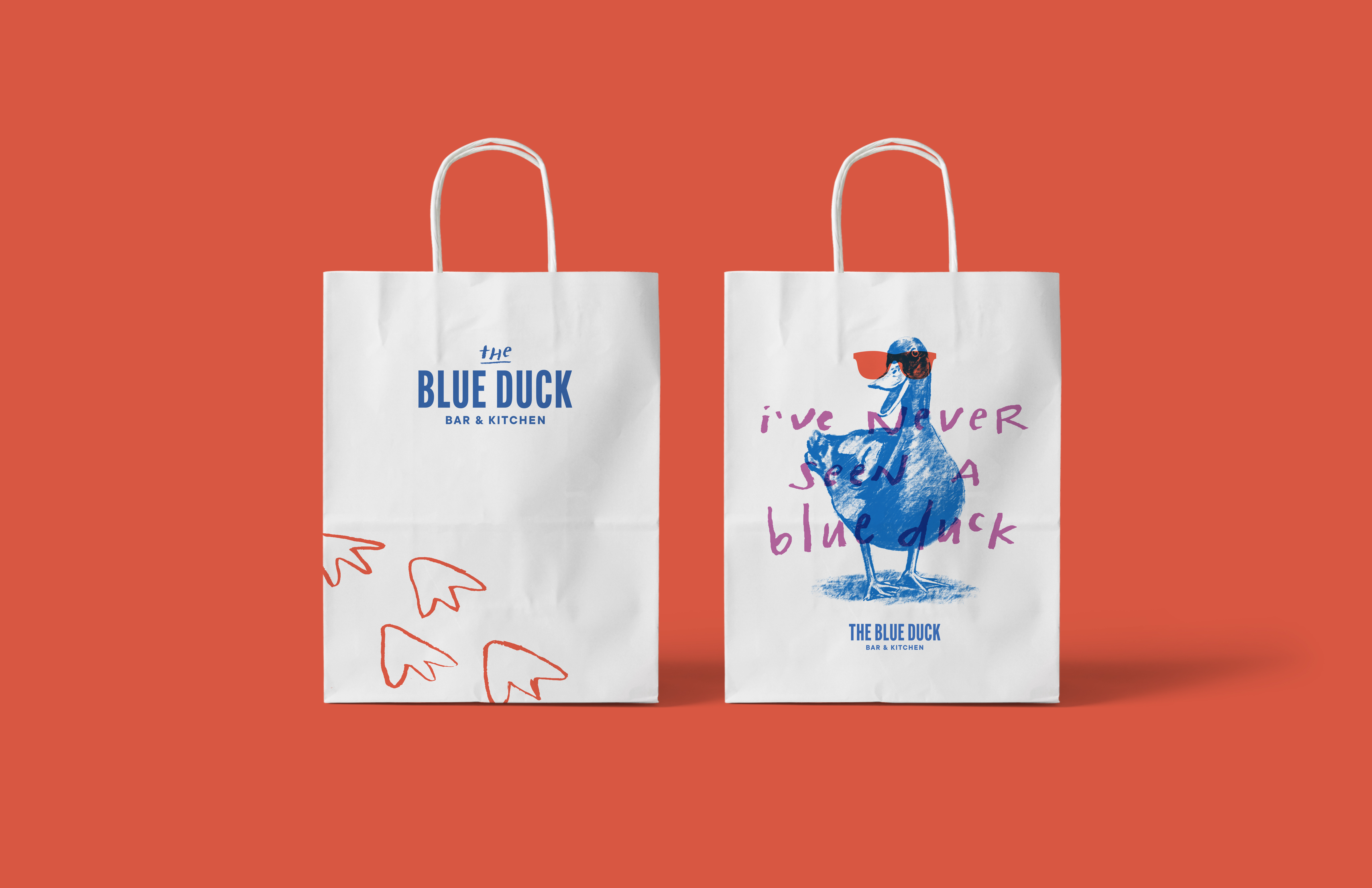 Photo of two paper shopping bags highlighting The Blue Duck branding through typography, illustration, and color accents, demonstrating the brand's visual identity on packaging.