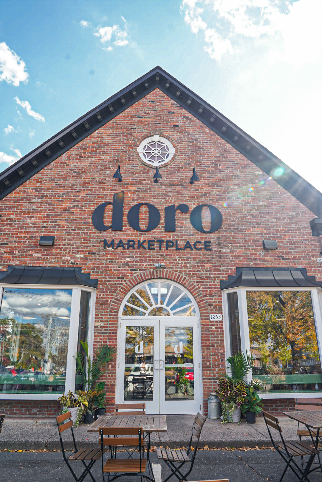 A photo of the Doro Marketplace storefront. The building has a charming brick facade with a distinctive arched doorway and large windows. The "Doro Marketplace" sign is prominently displayed above the entrance.