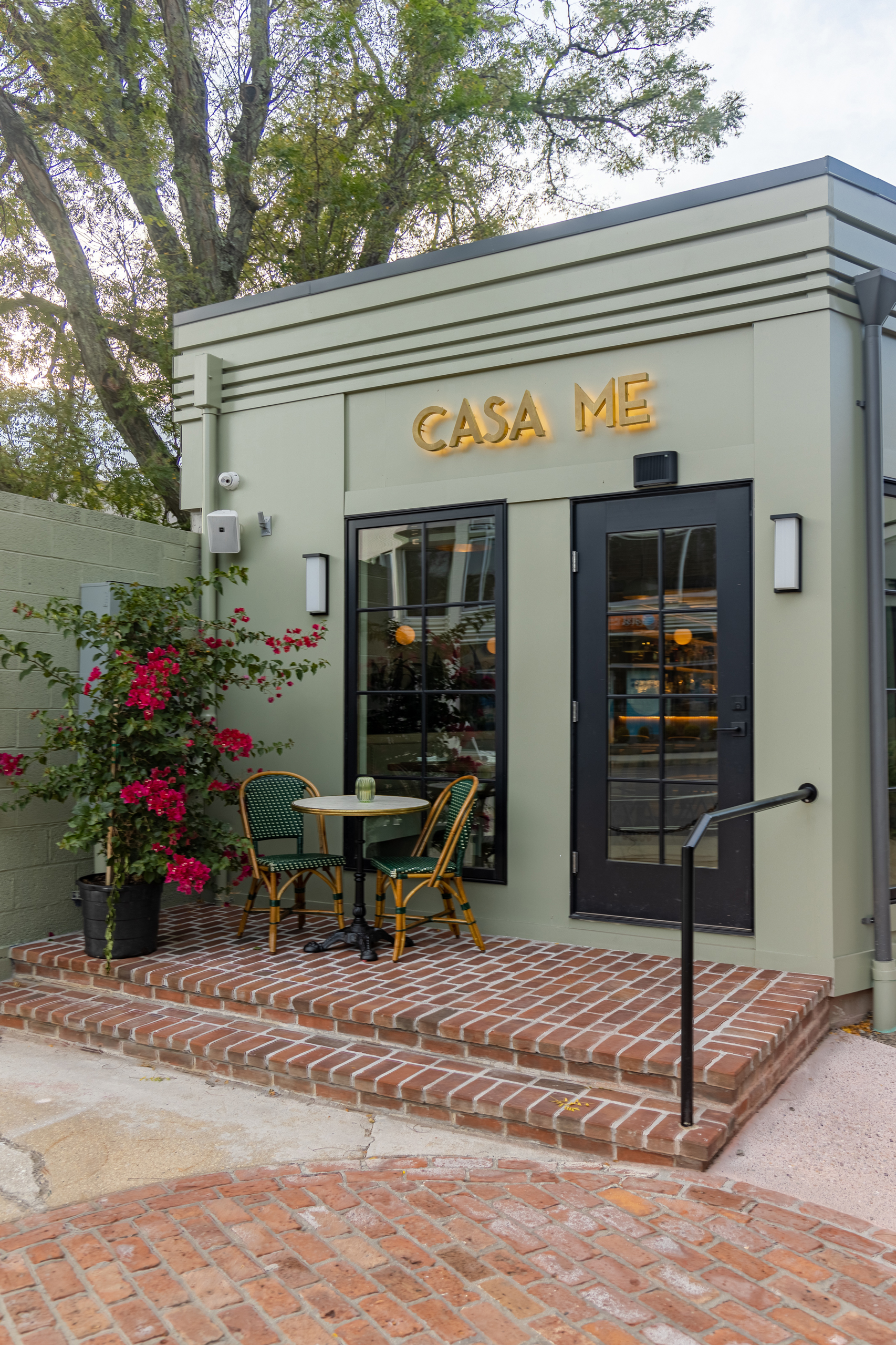 Exterior view of the Casa Me restaurant, featuring a modern building design with large windows, outdoor seating, and prominent signage, showcasing the restaurant's branding and architectural style.