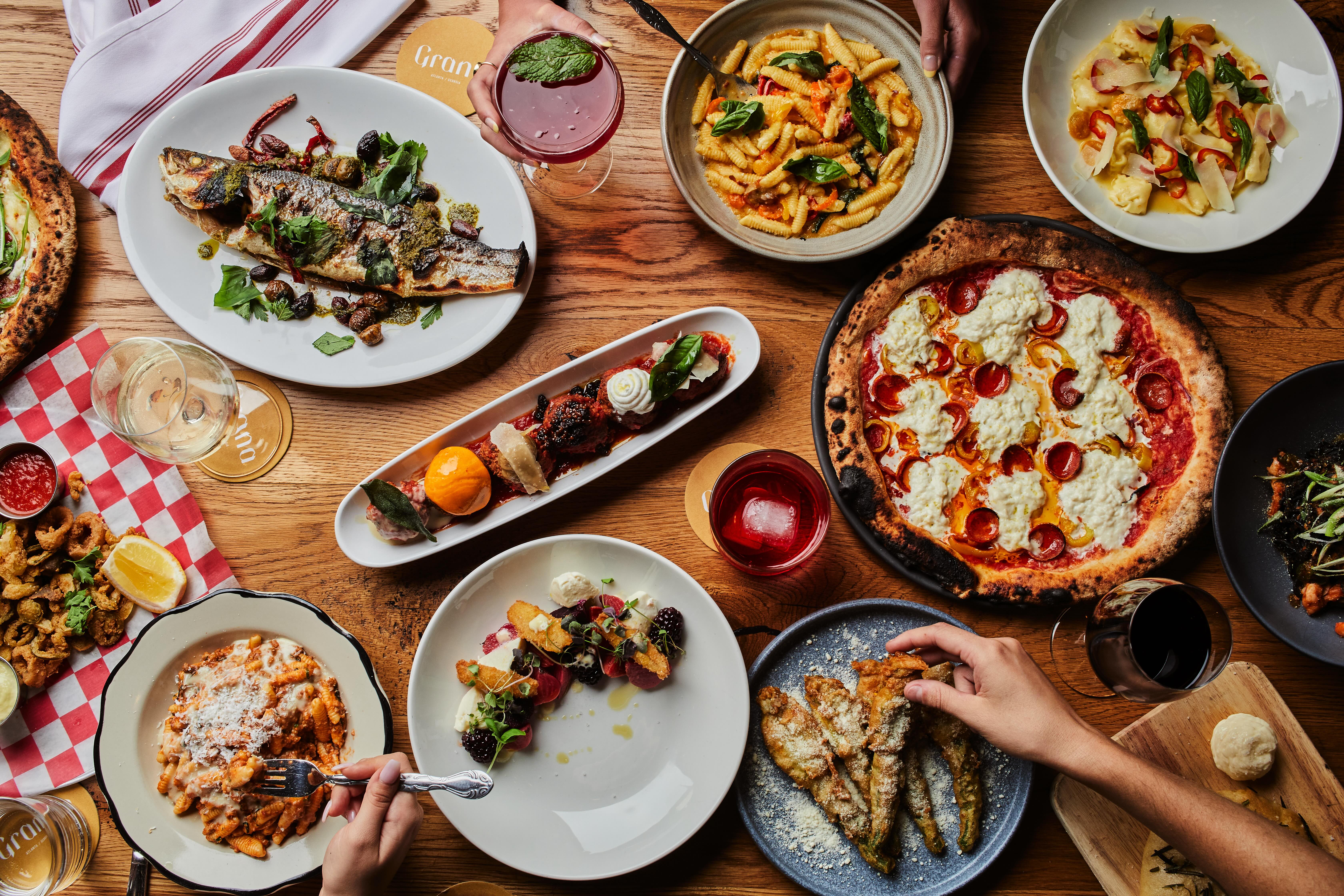 Overhead view of a beautifully styled table featuring an assortment of Italian cuisine, highlighting the vibrant colors and textures of the dishes, with hands adding a human element to the composition, suggesting a communal meal.