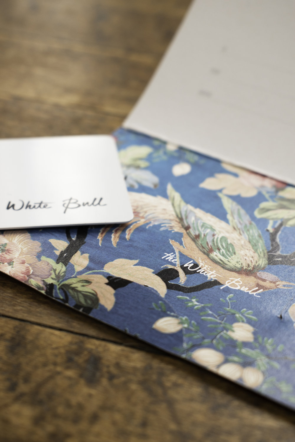 A close-up of The White Bull's stationery, featuring an open envelope lined with a blue floral pattern. The restaurant's name is written in a cursive script on both items.