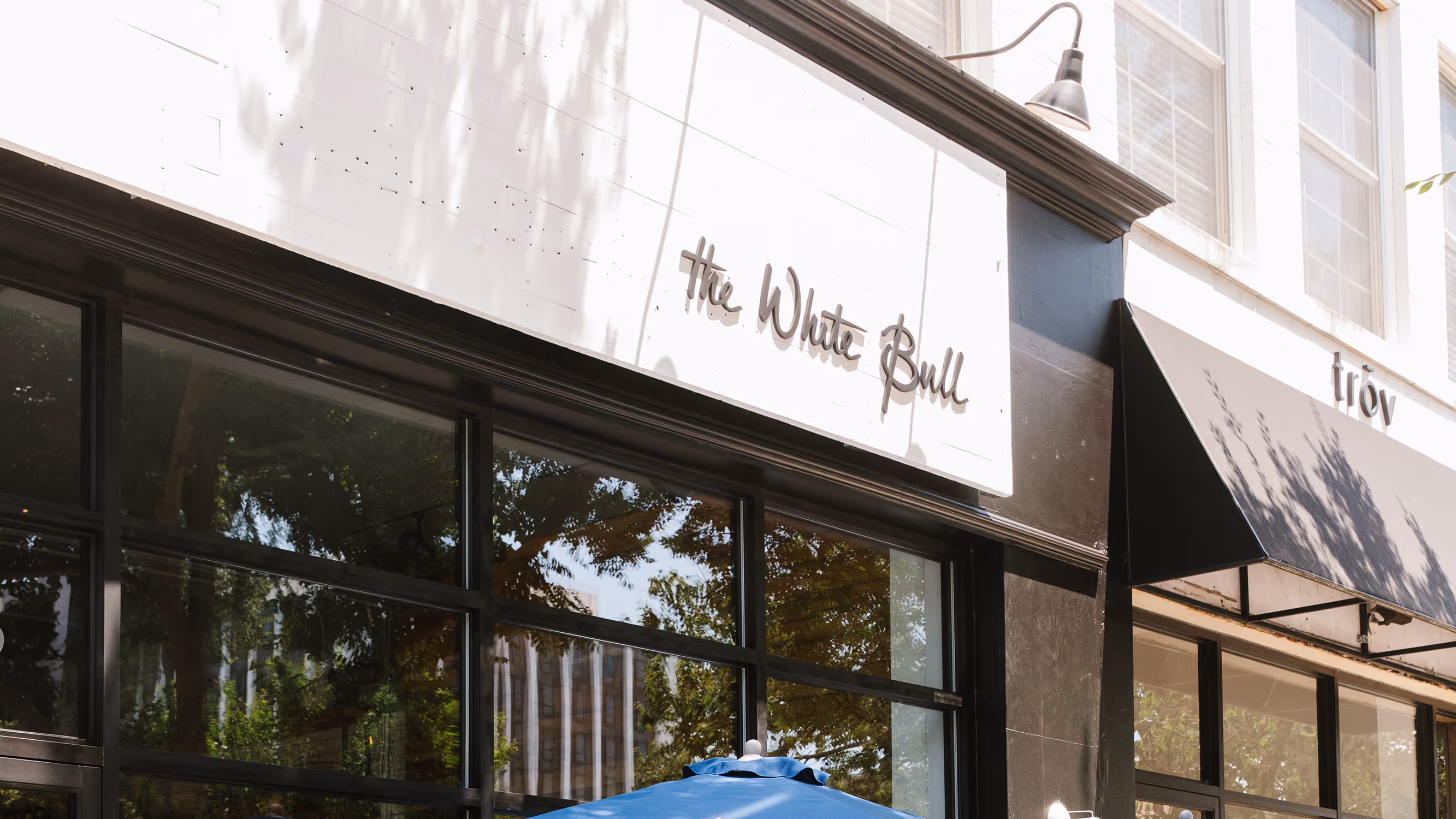The exterior of The White Bull restaurant, featuring a white sign with the restaurant's name in a cursive font above a glass storefront.