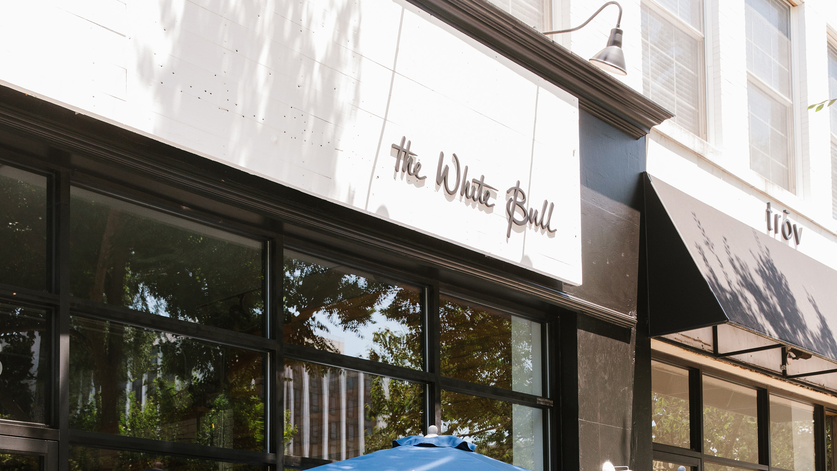 The exterior of The White Bull restaurant, featuring a white sign with the restaurant's name in a cursive font above a glass storefront.