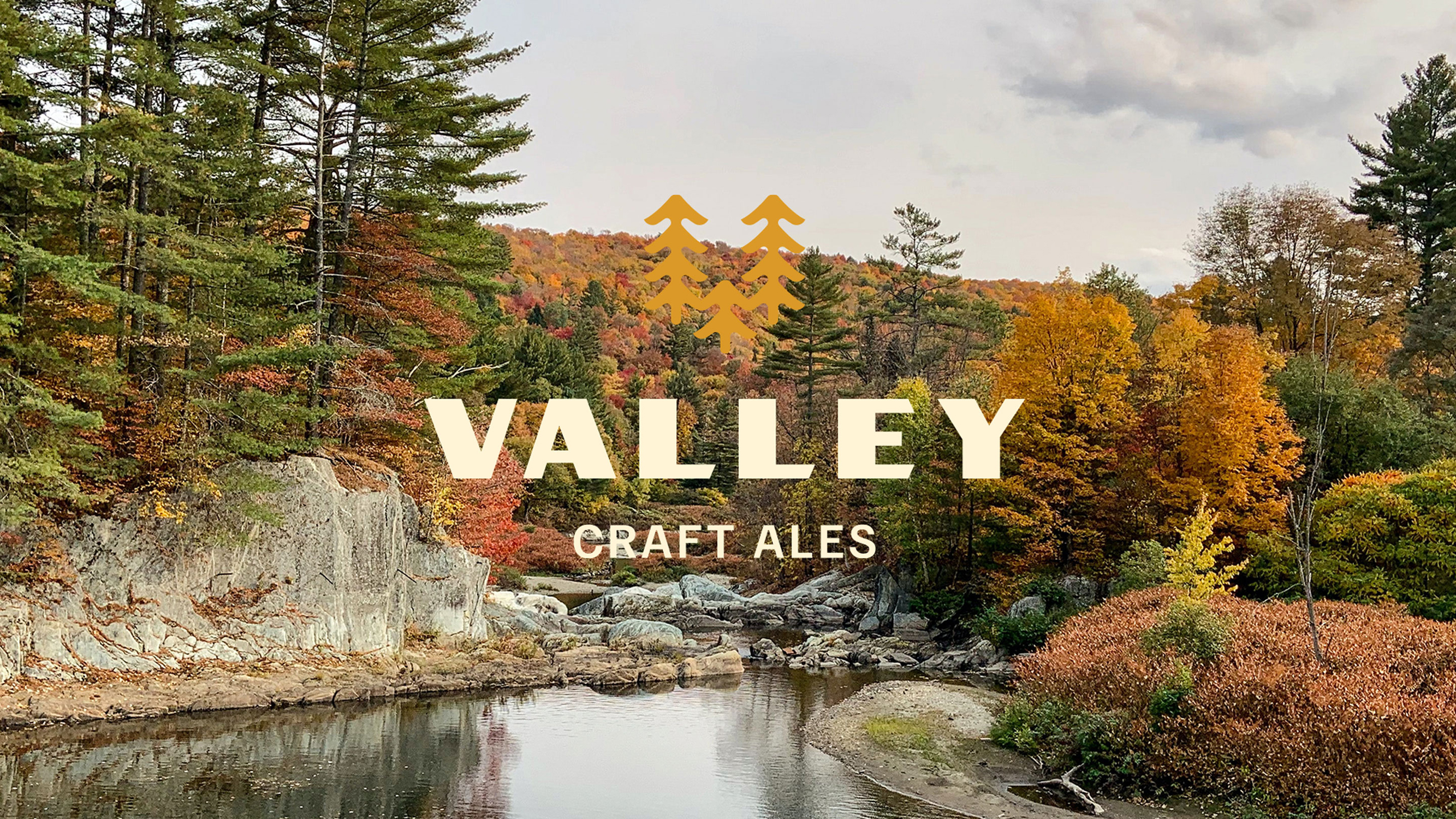 A scenic autumn landscape with a river flowing through colorful foliage, overlaid with the Valley Craft Ales logo in bold and a stylized pine tree icon.