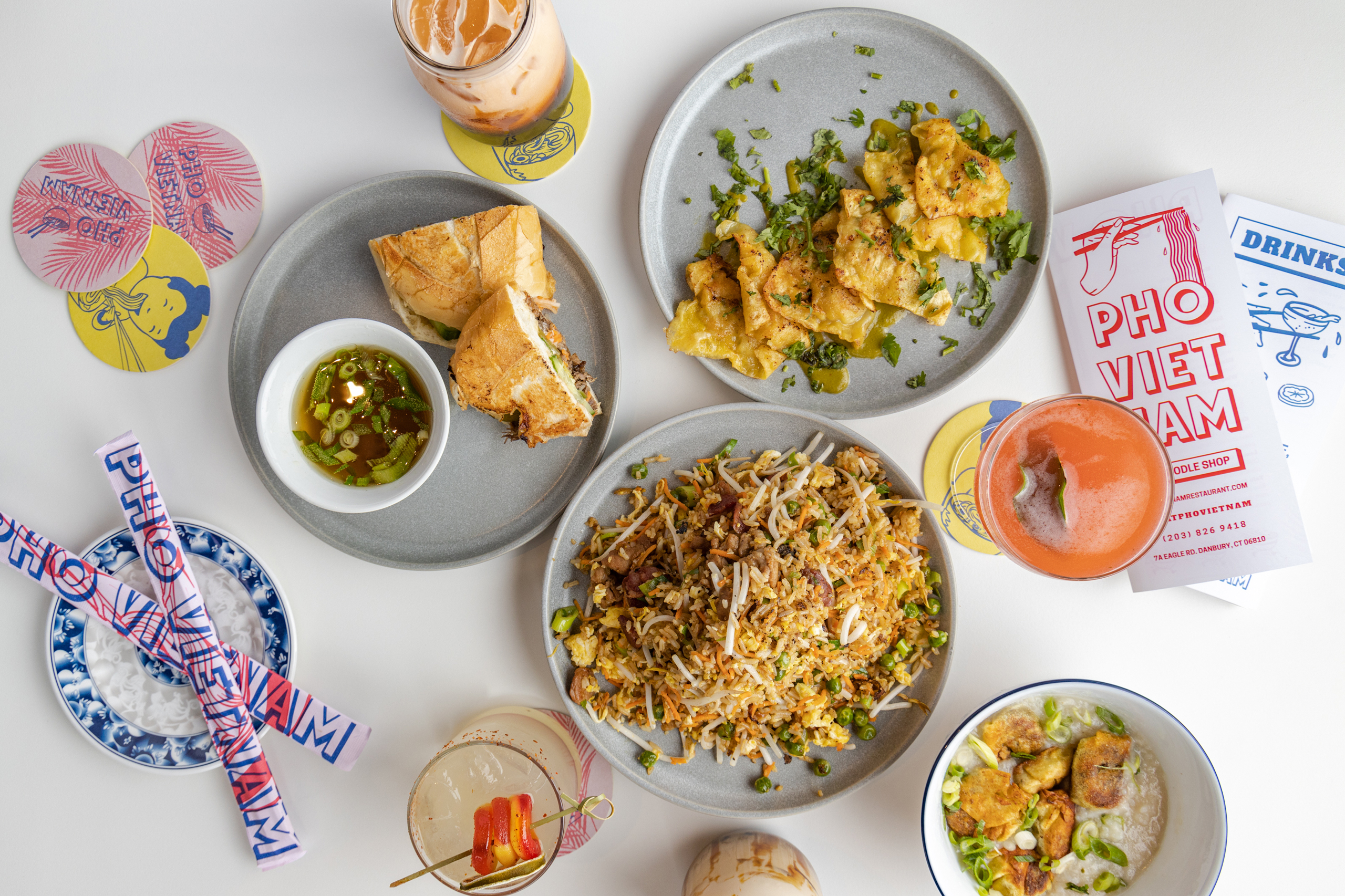 Stylized overhead shot of a Vietnamese food spread, showcasing the culinary offerings of Pho Vietnam alongside their branded materials, such as menus, coasters, and chopsticks, emphasizing a modern and inviting dining experience.