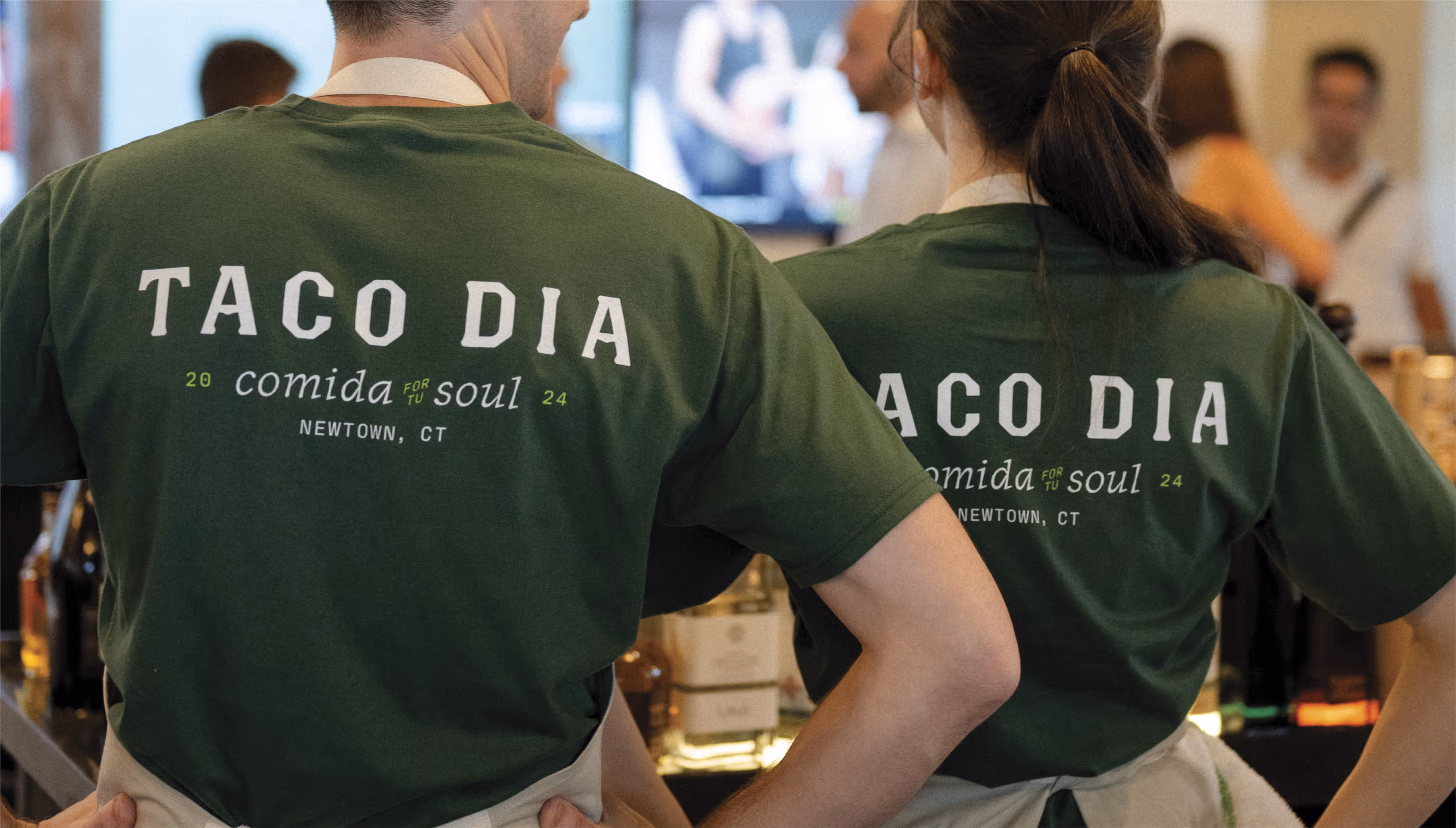 A photo of two bartenders wearing custom designed Taco Dia merchandise apparel shirts.