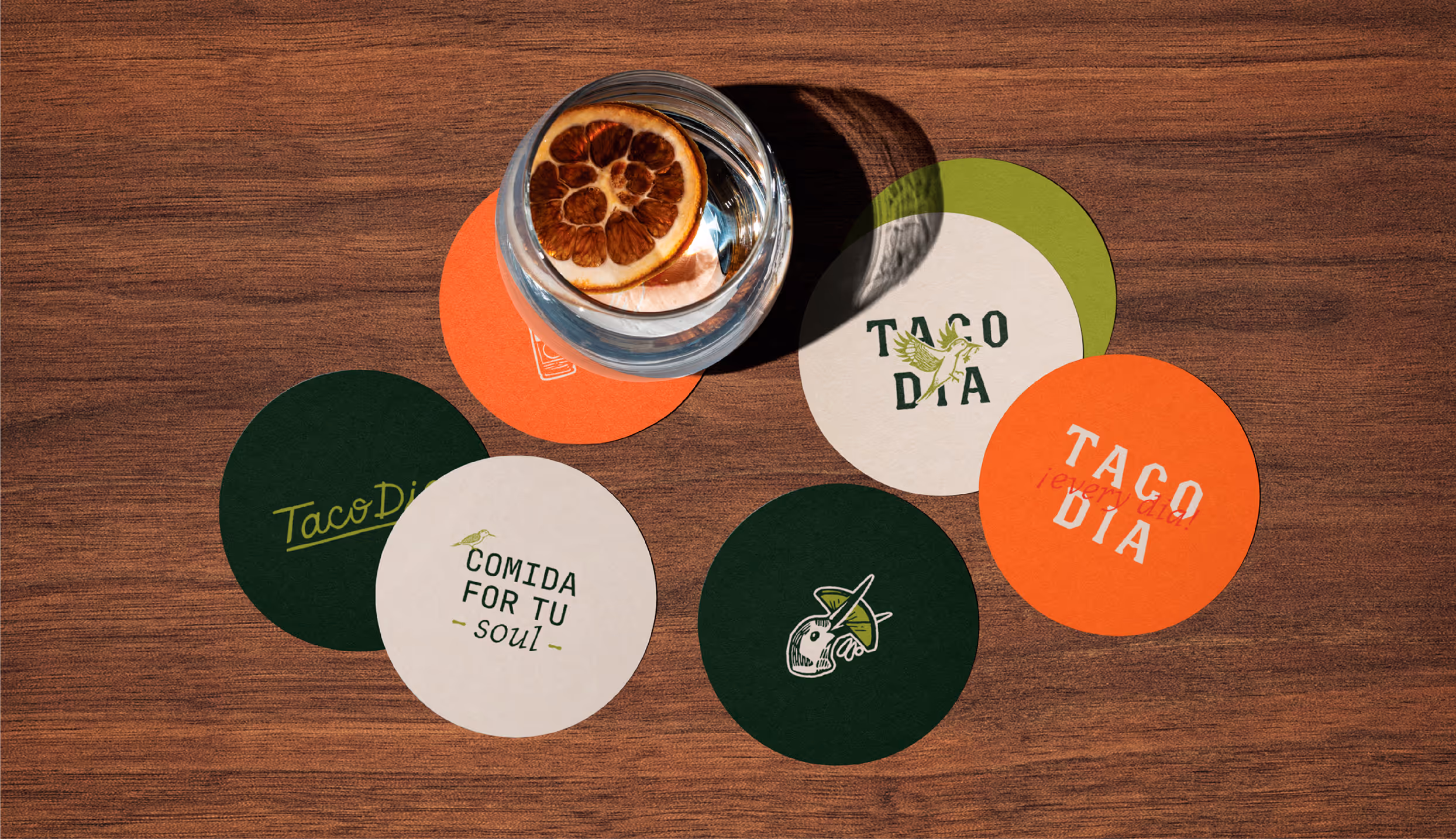 Various coasters on a wooden table with custom branding that tells the narrative of Taco Dia and the bird illustration, Taquito.
