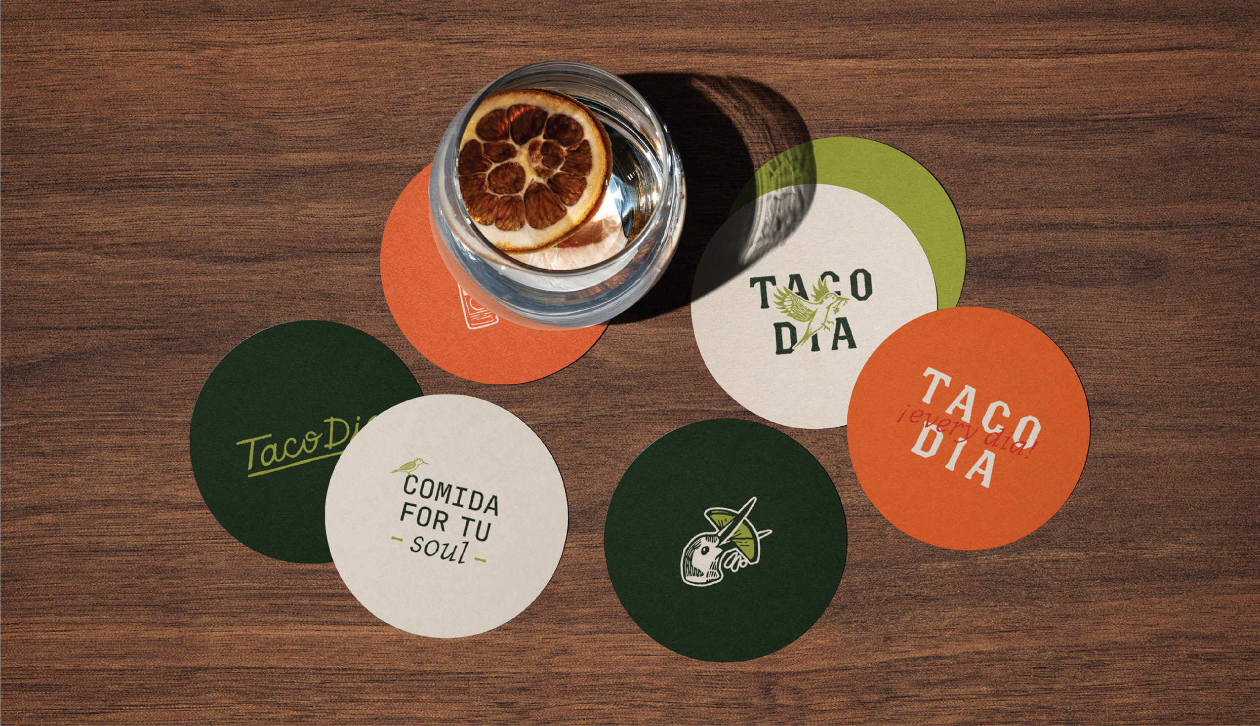 Various coasters on a wooden table with custom branding that tells the narrative of Taco Dia and the bird illustration, Taquito.