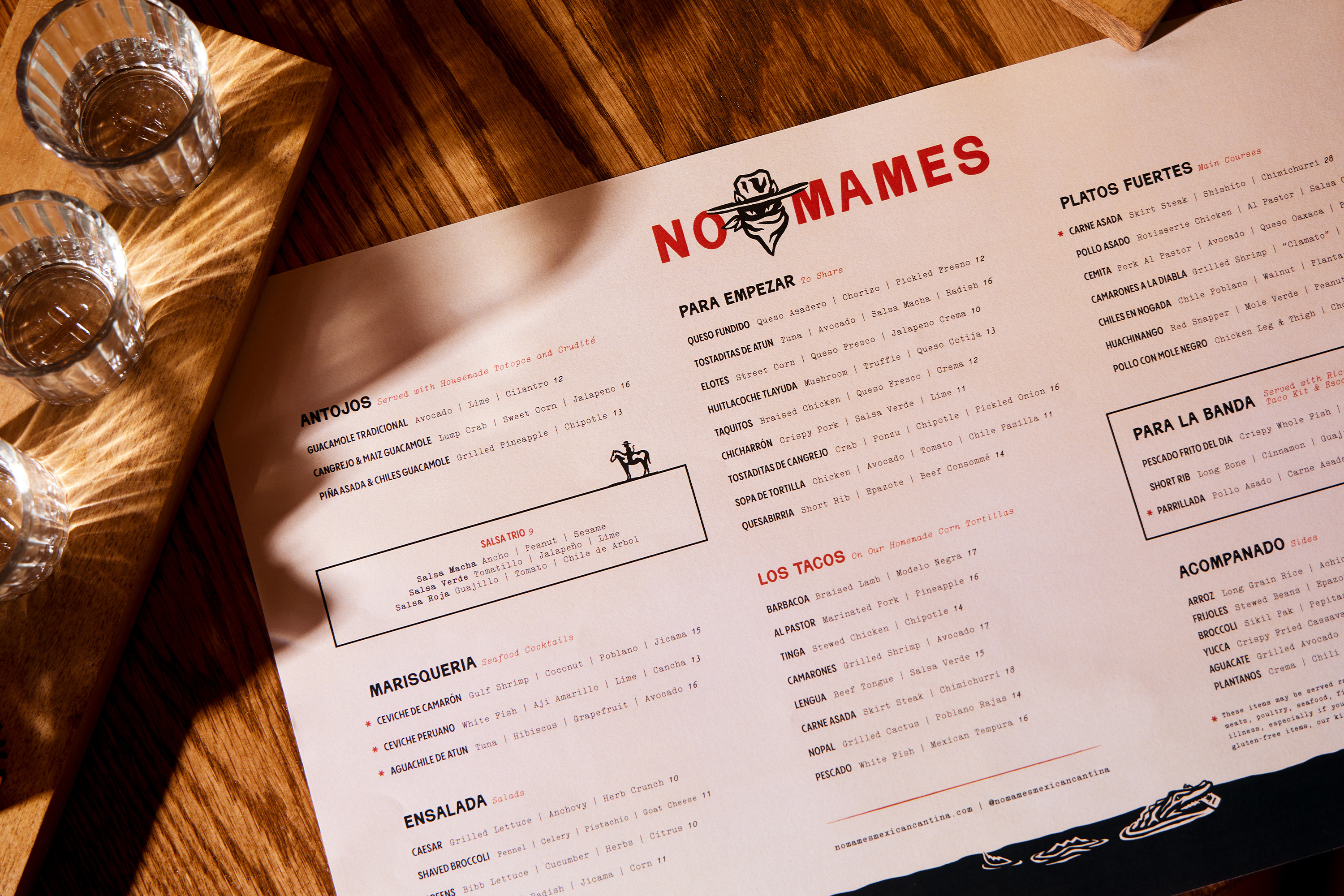 The logo features a stylized illustration of a person wearing a wide-brimmed hat and a mask, with the text "No Mames" integrated into the design.