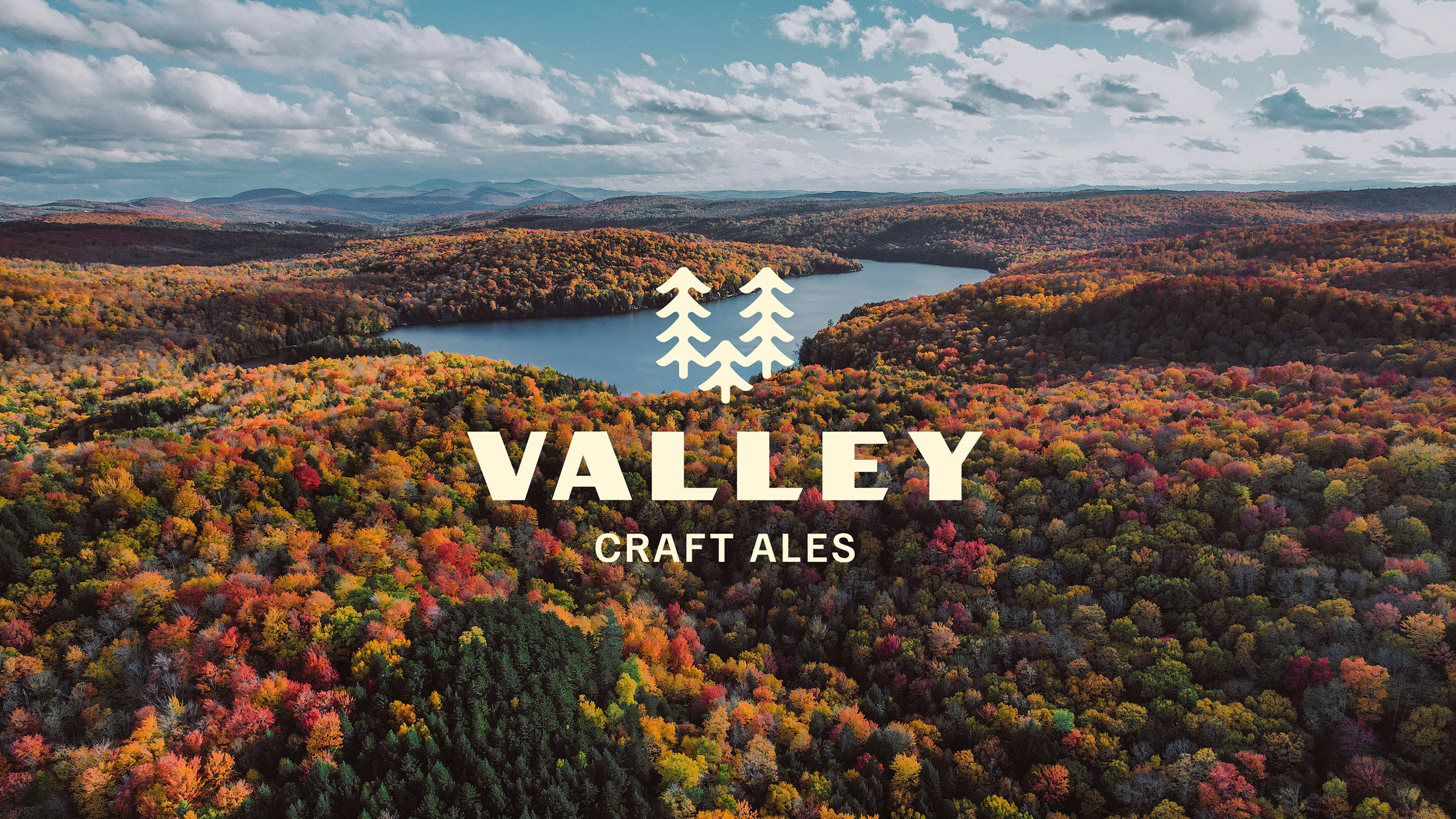 A scenic autumn landscape with a river flowing through colorful foliage, overlaid with the Valley Craft Ales logo in bold and a stylized pine tree icon.