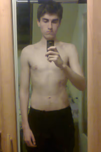 Young man taking a shirtless mirror selfie with a phone in a wooden door frame.