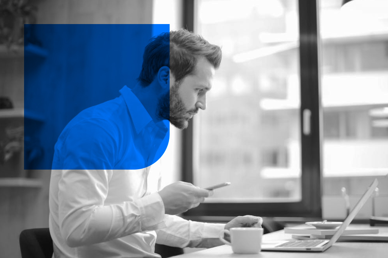 Professional working at desk with laptop and coffee, using smartphone