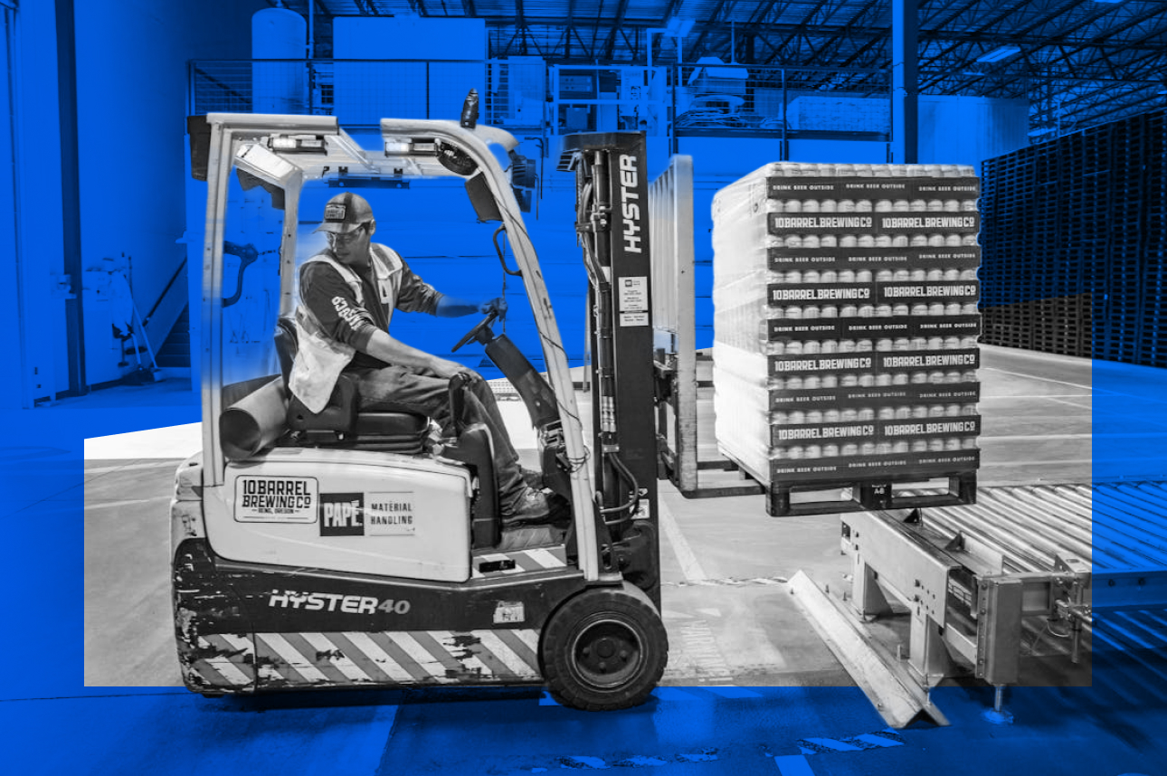 Forklift operator moving stacked beer cases in a blue-tinted warehouse