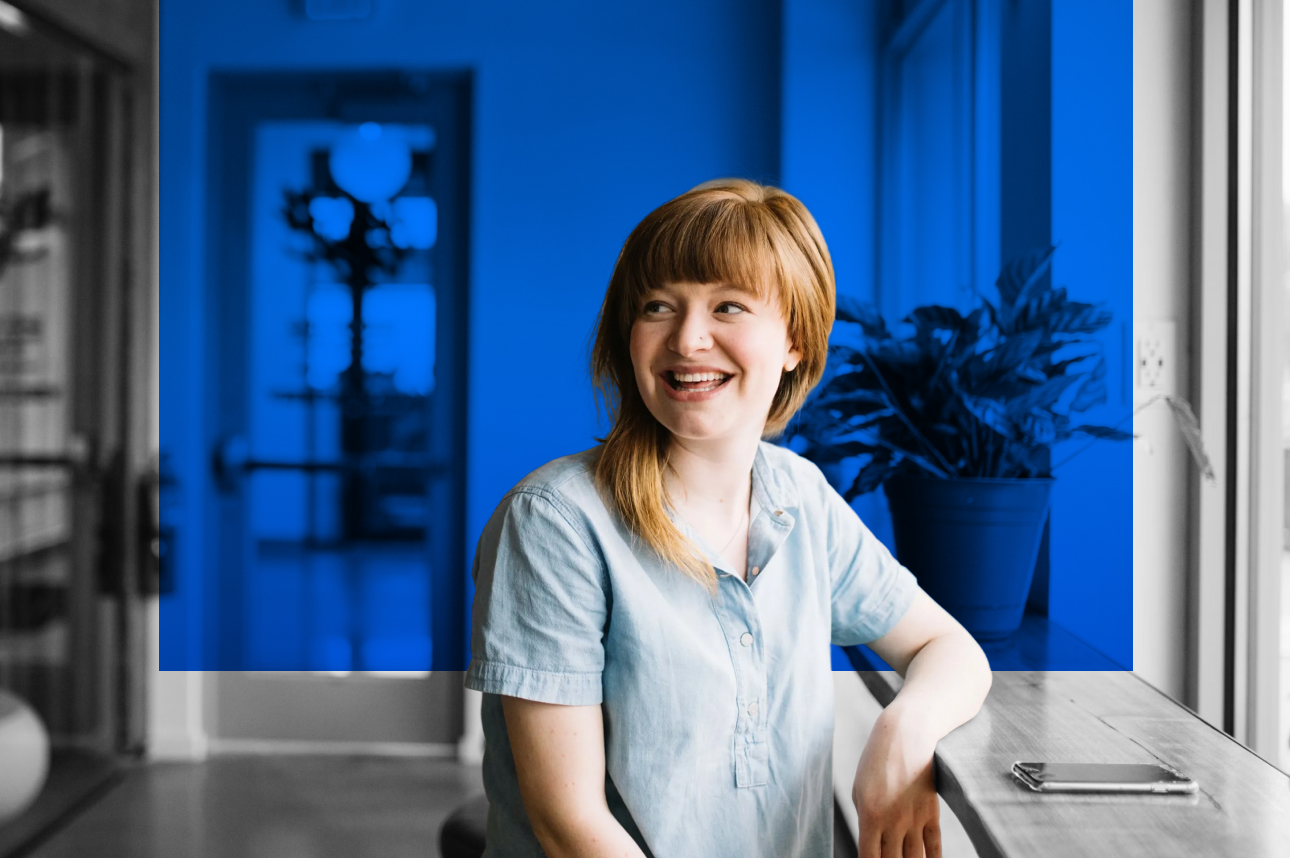 Person in light blue shirt smiling at desk with blue background