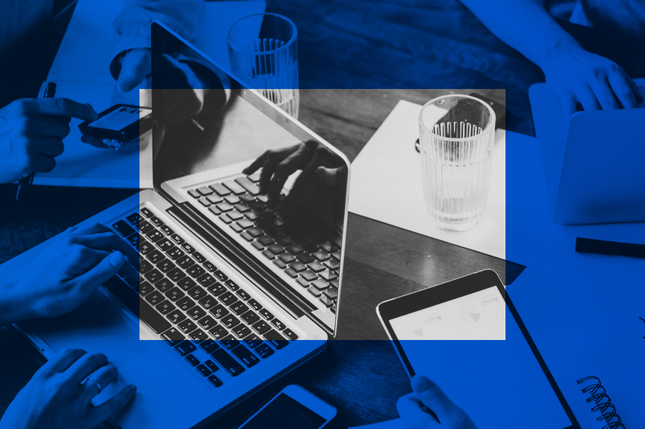 Laptop, smartphone, and water glass on desk with blue-tinted workspace background