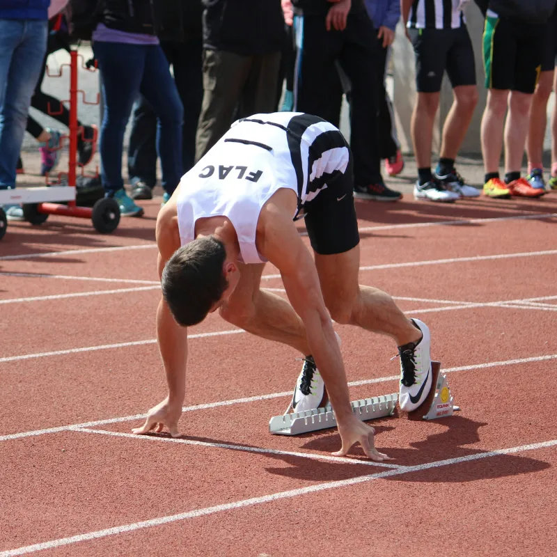 Low-angle view of a female fencer in white fencing gear holding a foil against a clear blue sky.