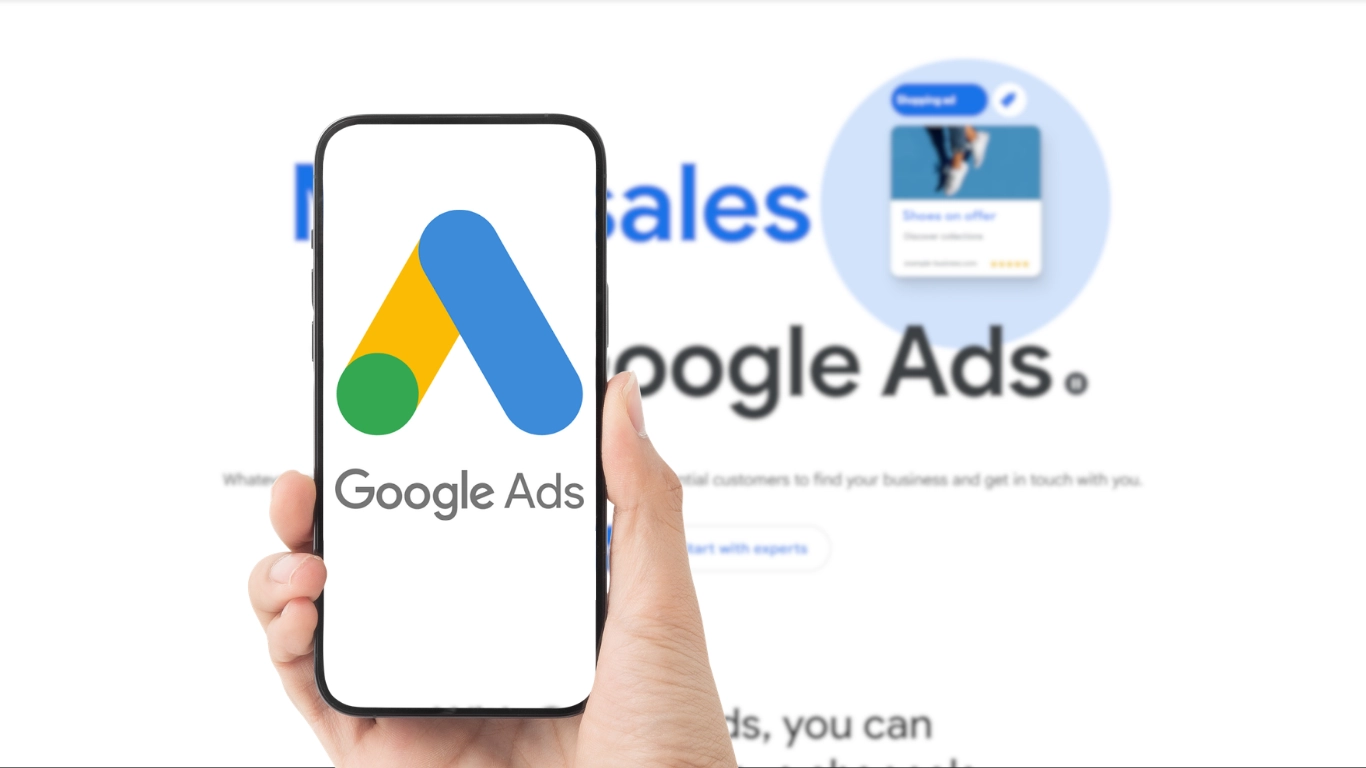 Hand holding a smartphone displaying the Google Ads logo with the Google Ads website visible in the background