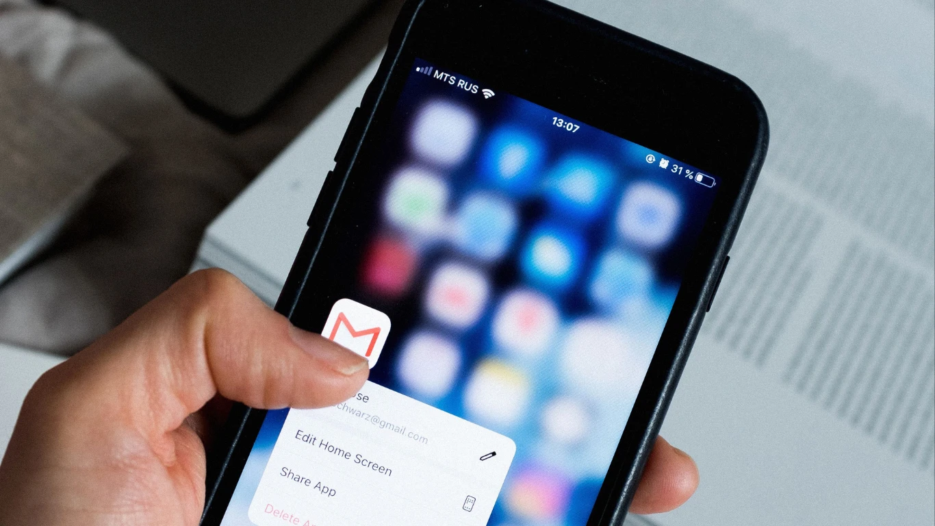 Hand holding a black iPhone with the Gmail app icon visible on the home screen