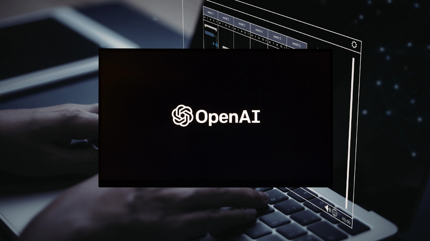 OpenAI logo displayed on a dark screen overlay above a person typing on a MacBook laptop