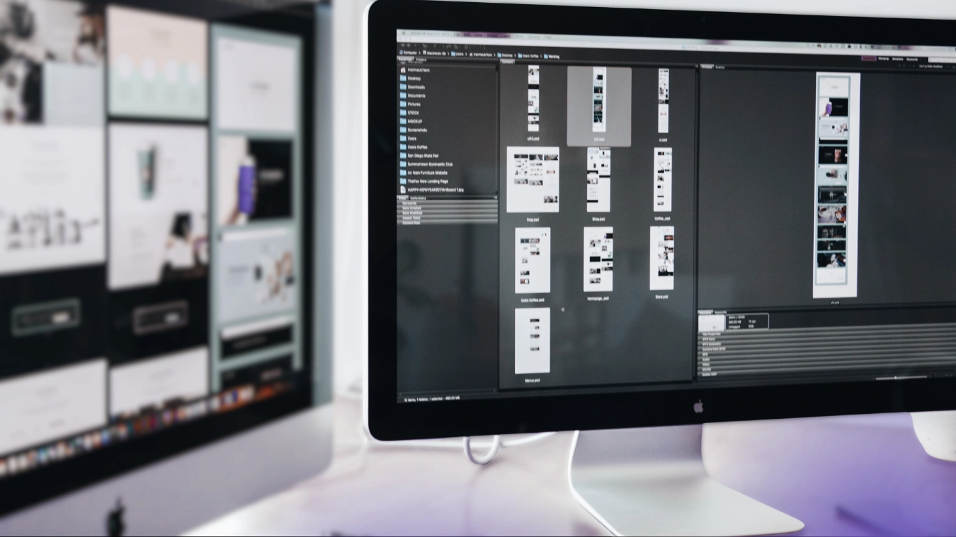 Apple iMac displaying a file manager with multiple website wireframe and design files, with a second monitor showing website layouts in the background