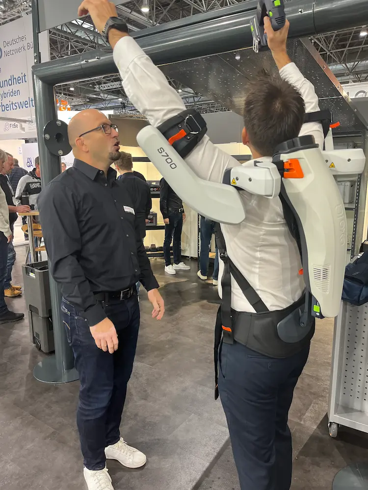 A trade show attendee tests the S700 shoulder exoskeleton while performing overhead tasks