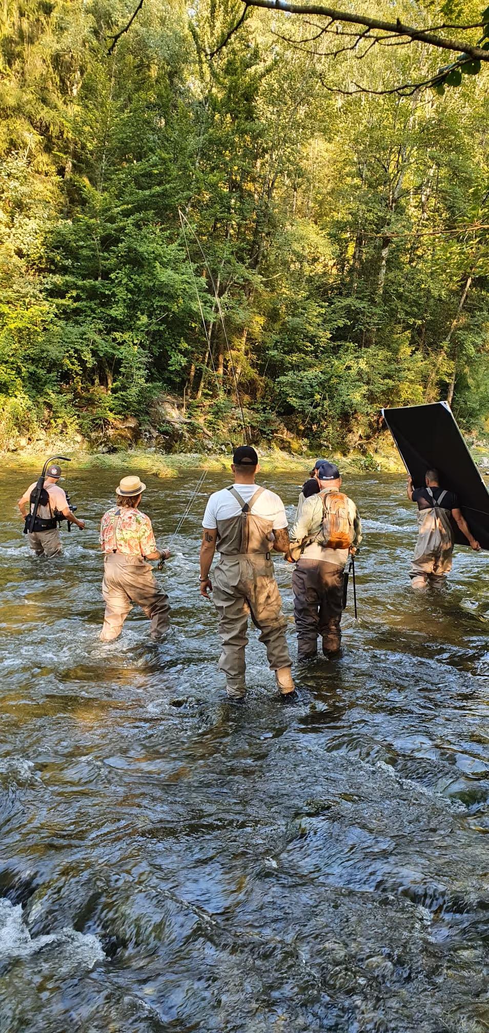 Fünf Personen mit Watthosen stehen in einem Fluss und angeln vor einem grünen Wald.