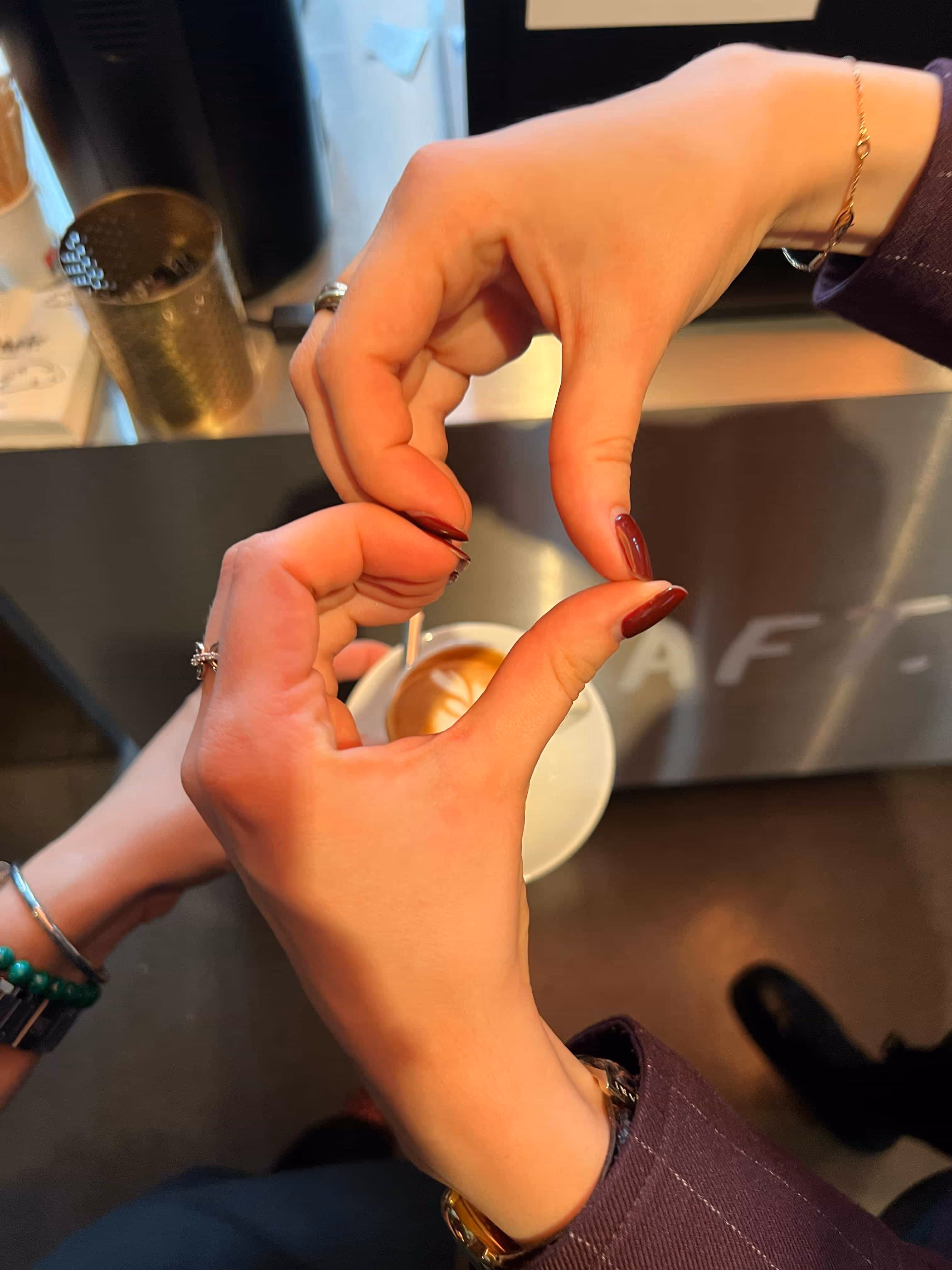 Zwei Hände formen ein Herz vor einer Kaffeetasse auf einem Tresen.
