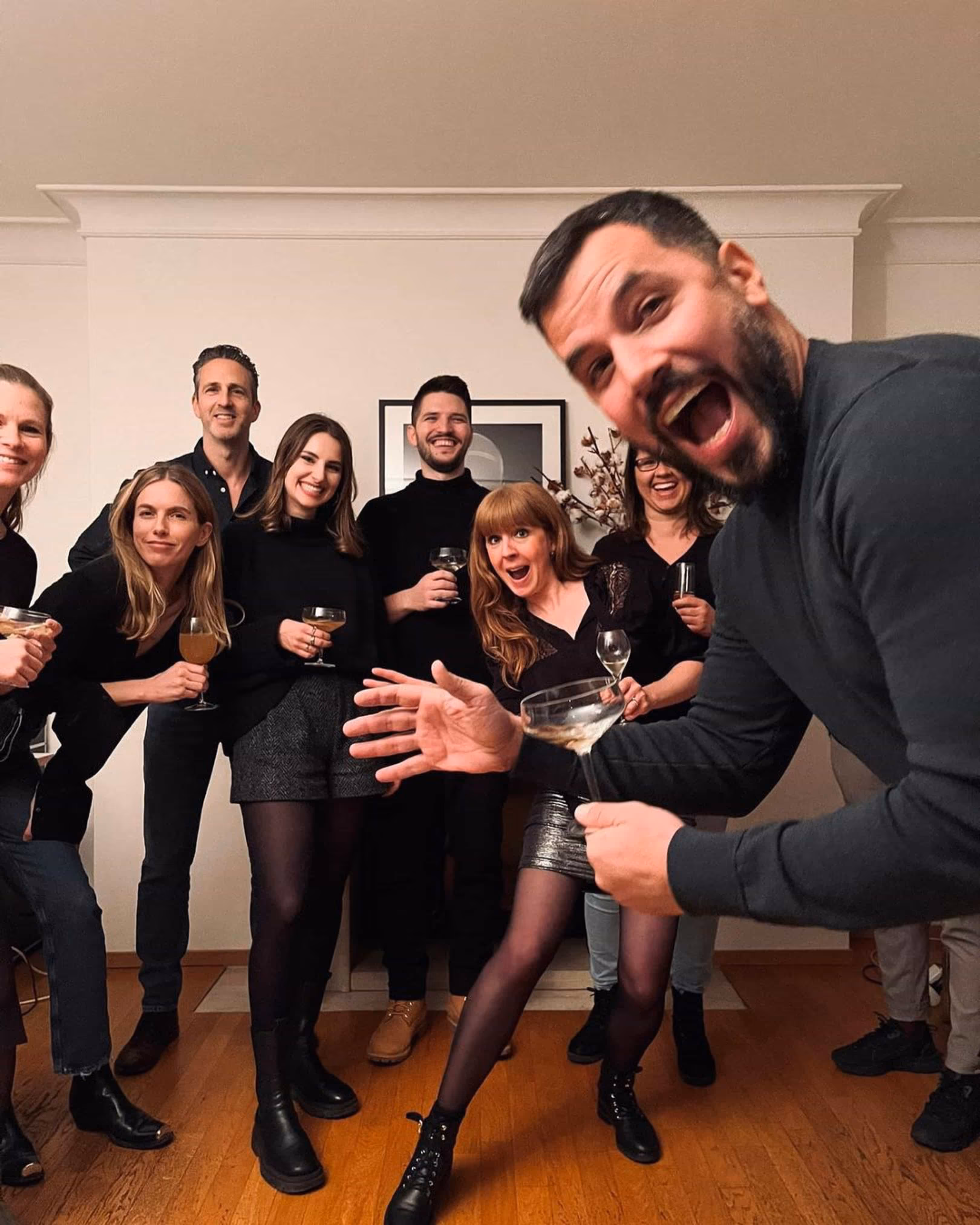 Gruppe fröhlicher Menschen, die zusammen in einem Raum mit Getränken anstossen und lachen.