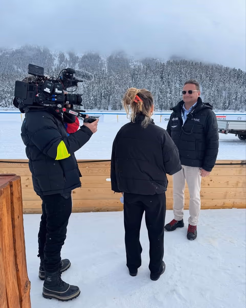 Eine Kamera-Crew filmt im Schnee ein Interview zwischen einem Mann mit Sonnenbrille und einer Frau mit zurückgebundenem Haar vor einem schneebedeckten Wald.