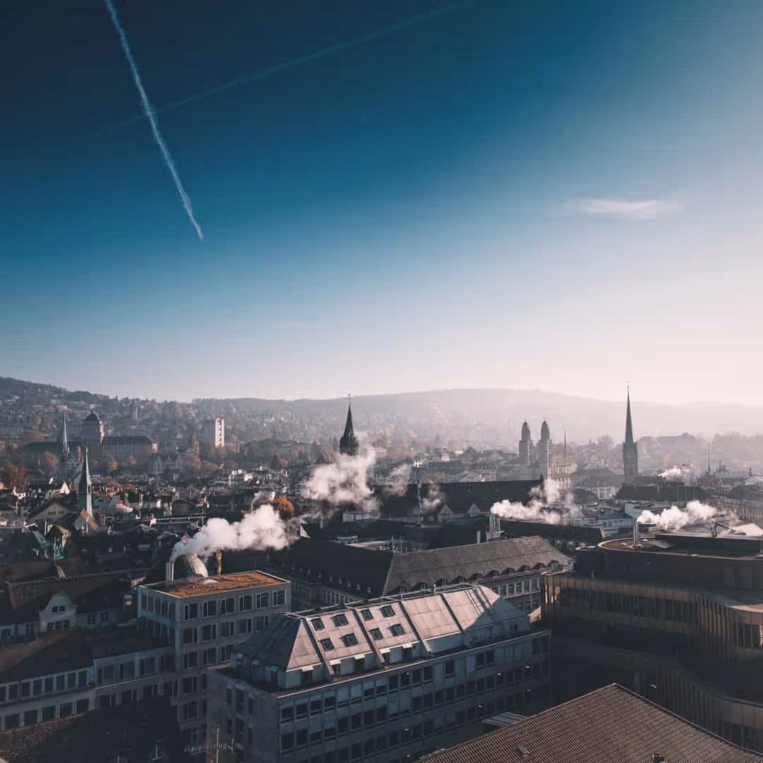 Stadtansicht mit Kirchtürmen und Gebäuden unter klarem Himmel mit Kondensstreifen.