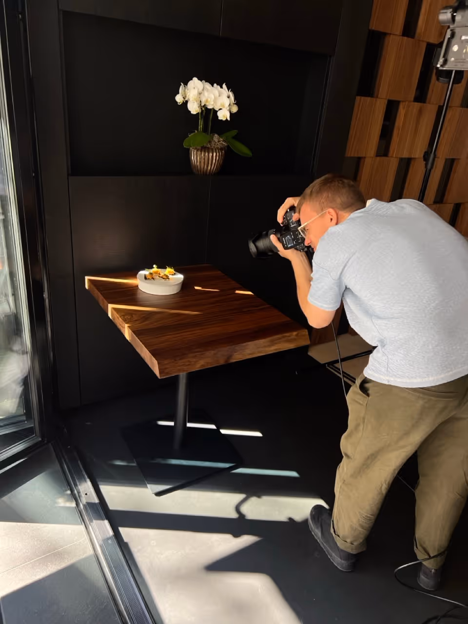 Fotograf macht ein Foto von einem dekorativen Teller auf einem Holztisch in einem modernen Raum mit Orchidee.