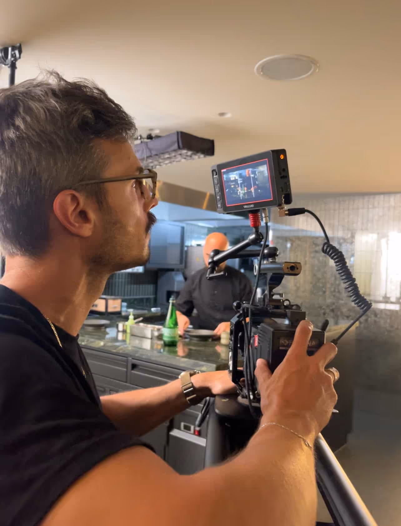 Kameramann mit Brille filmt einen Koch, der in einer modernen Küche arbeitet.