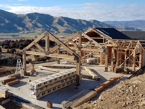 A centeral otago construction site where hardwood beams trusses recycled from old wharf is being put up as the frame of the house is built around it.