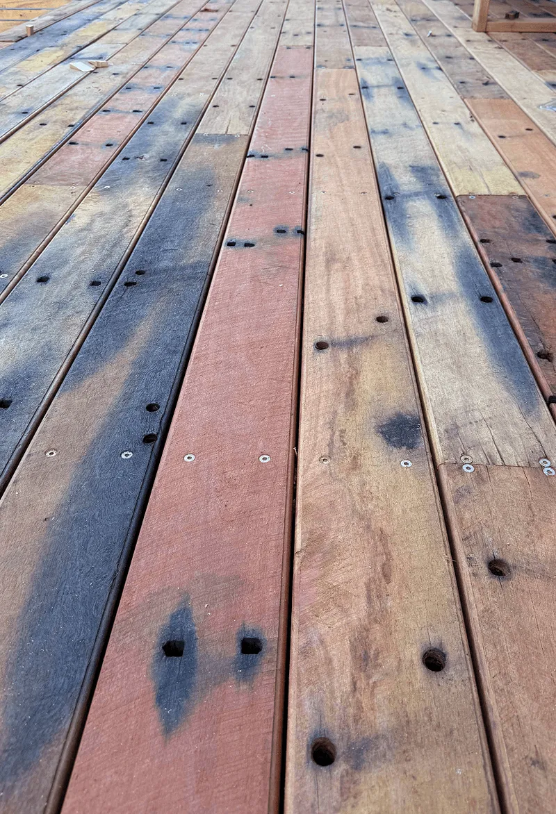 Close-up of weathered recycled wooden decking boards with varied colors and visible screw holes.