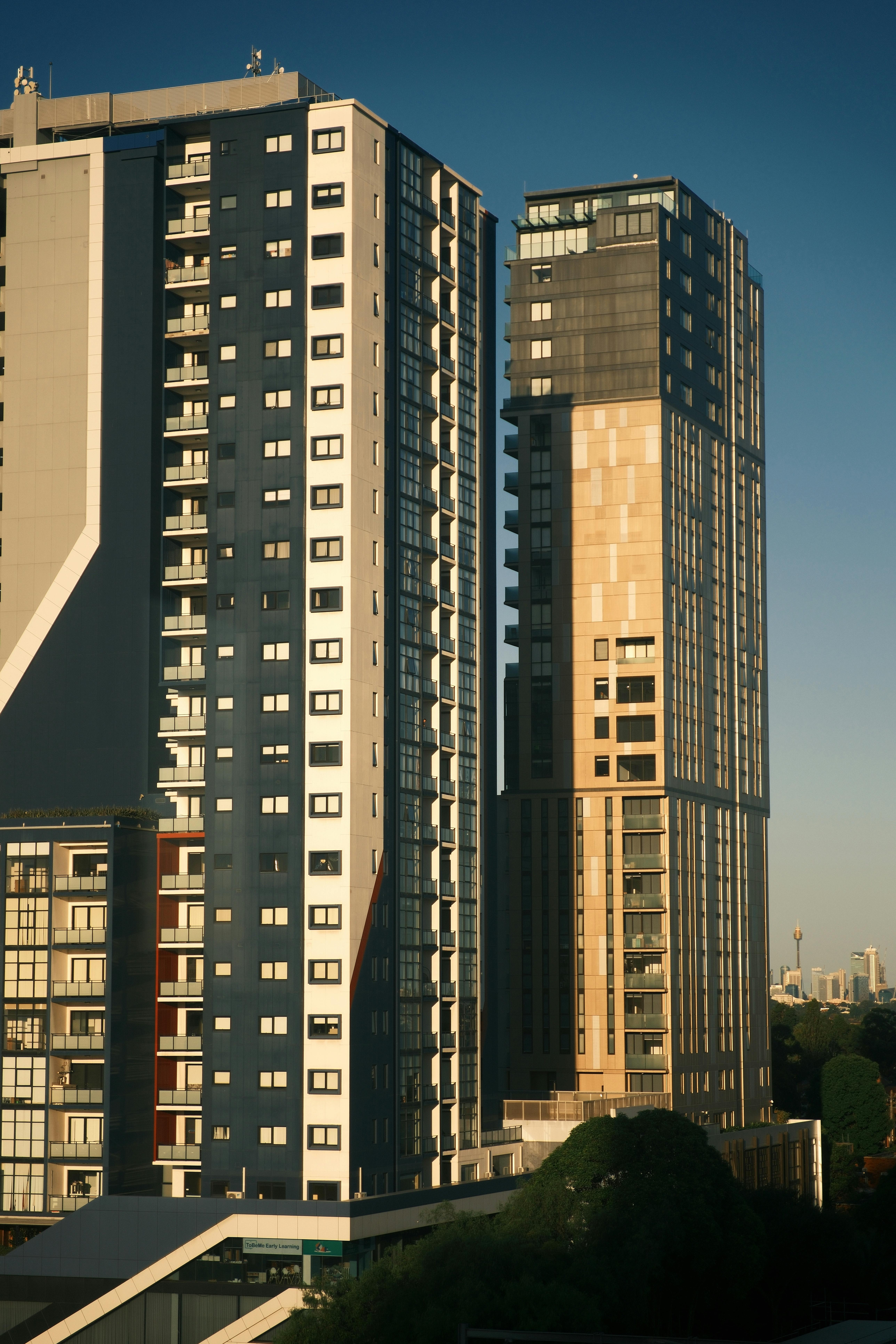 Two modern high-rise residential buildings illuminated by evening sunlight against a clear blue sky.