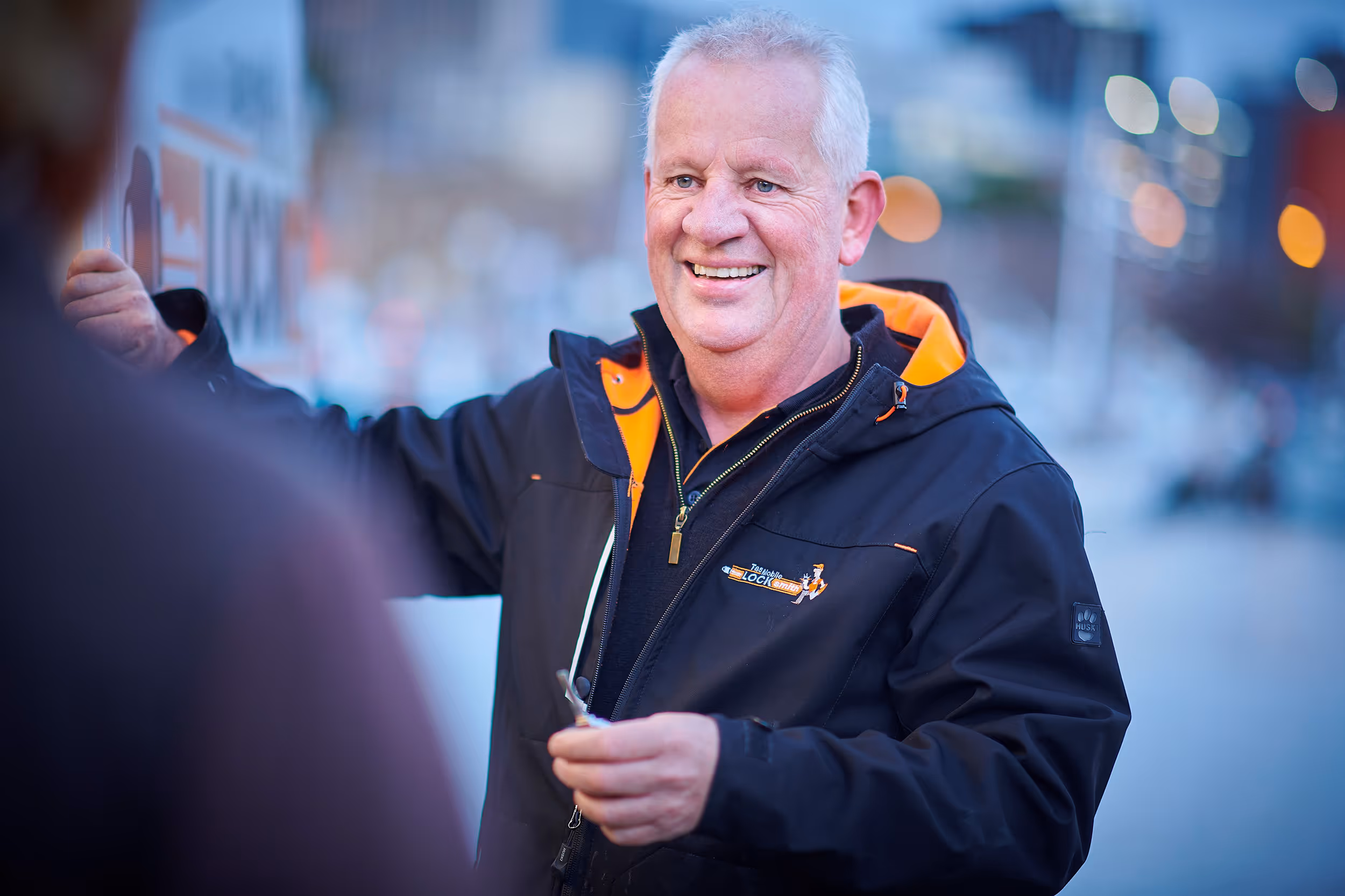 Smiling older man in black and orange jacket outdoors